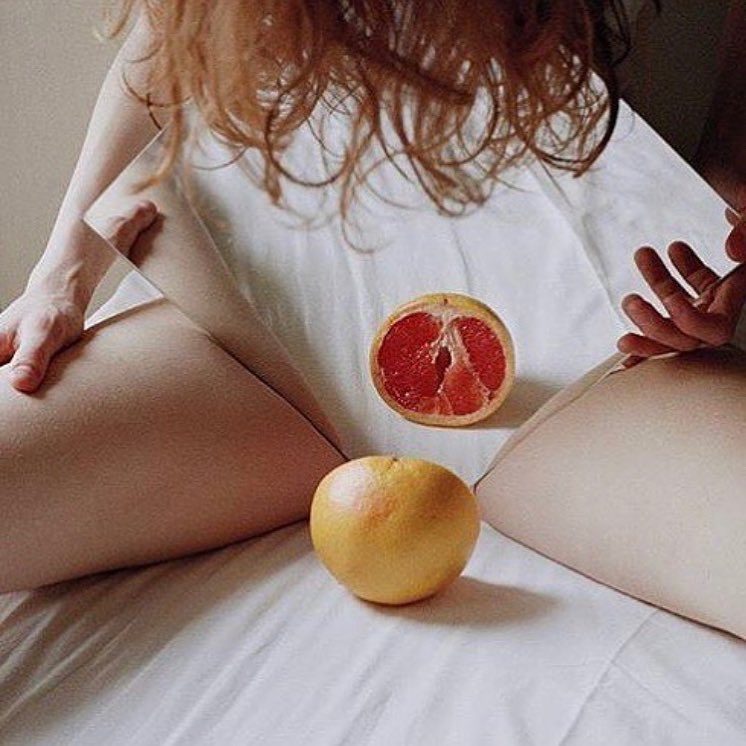 A woman sitting on white sheets holding a halved grapefruit