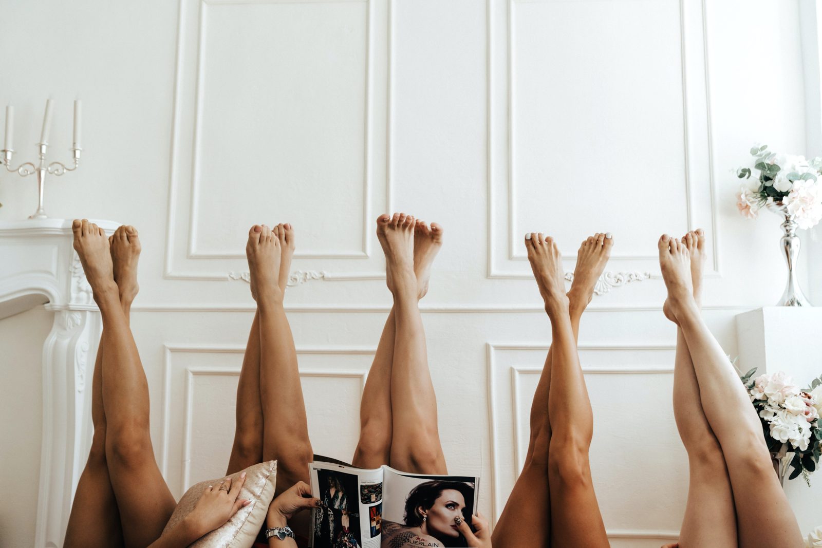 Women lying with their legs up against a white wall